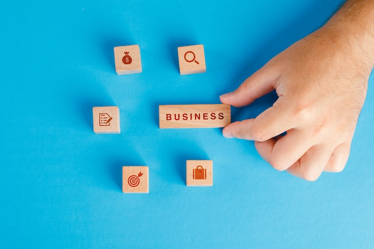 business-concept-with-icons-wooden-cubes-blue-table-flat-lay-hand-holding-wooden-block_176474-9353